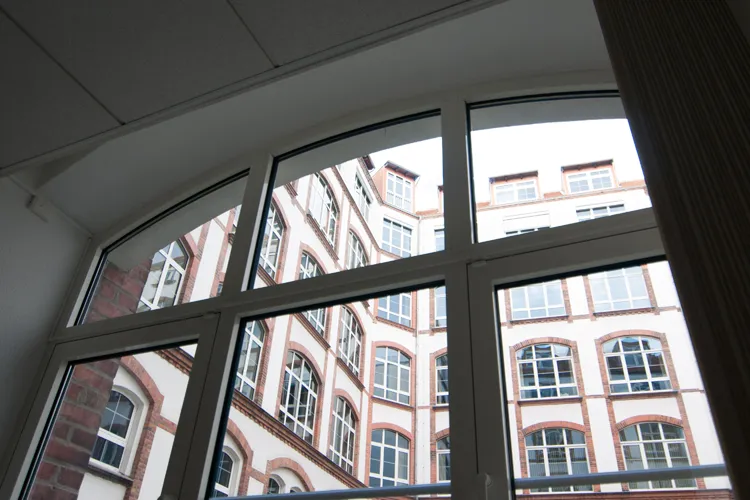 Blick durch ein Rundbogenfenster der Praxis auf Backsteinfassaden